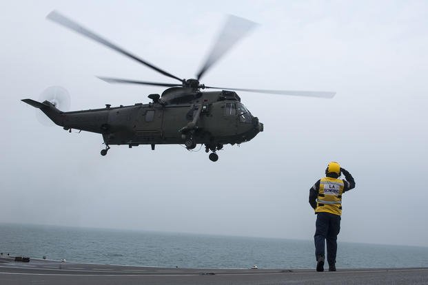 A British aircraft carrier crewman salutes a Royal Navy WS-61 “Sea King” helicopter as it departs the deck of the HMS Illustrious in the North Sea on April 3, 2014.