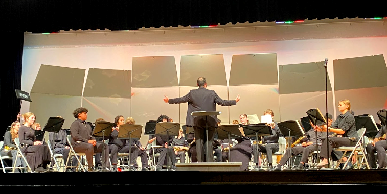 The conductor stands in front of the band members, directing a masterful performance.